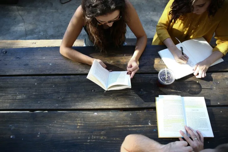 pessoas conversando e lendo em uma mesa em uma área externa
